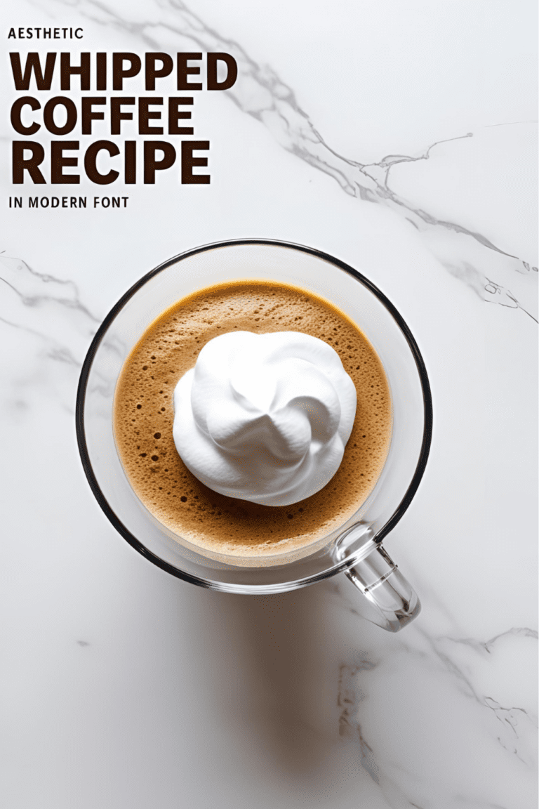 Glass of whipped coffee with fluffy top sitting on a white countertop, perfect for a morning pick-me-up.