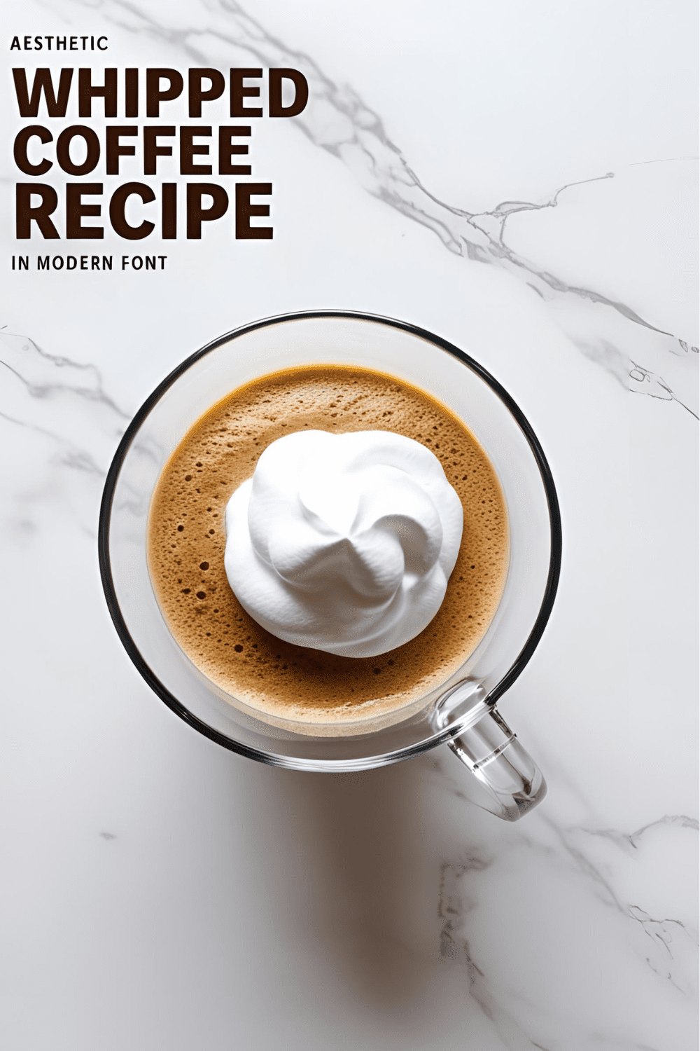 Glass of whipped coffee with fluffy top sitting on a white countertop, perfect for a morning pick-me-up.