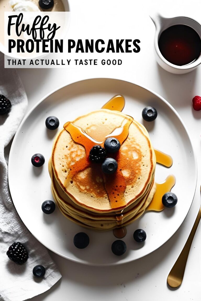 Stack of fluffy protein pancakes topped with berries and drizzled with maple syrup on white plate