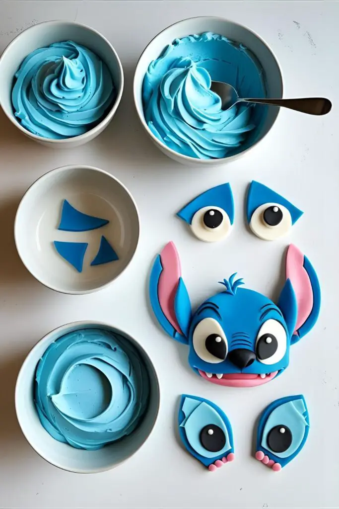 A flat-lay photo of supplies for a Stitch cake, including blue buttercream frosting and fondant pieces for the ears, eyes, and nose.