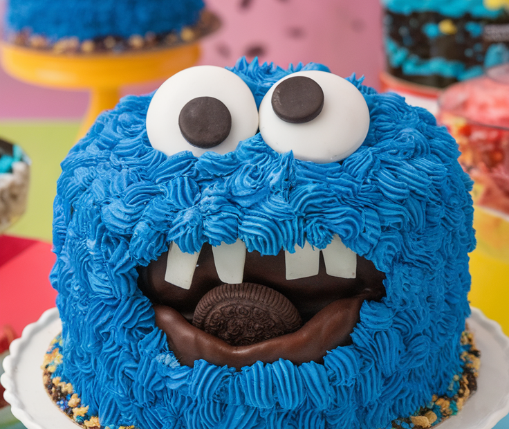 A fun, furry blue Cookie Monster cake with a cookie in its mouth and the text overlay "The Ultimate Cookie Monster Cake Tutorial!".