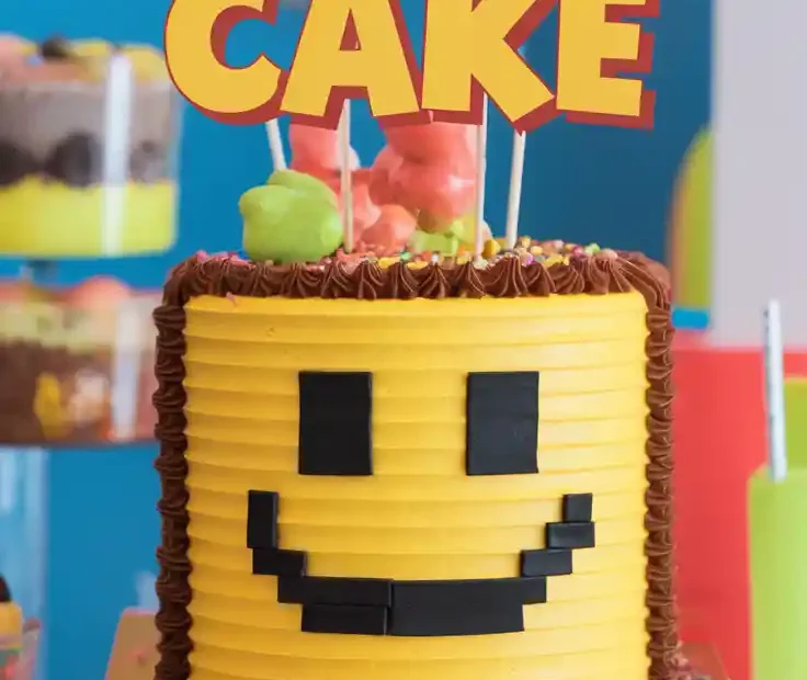 A fun yellow cake decorated like a Roblox Noob face with the text overlay "The Ultimate Roblox Cake Tutorial!".