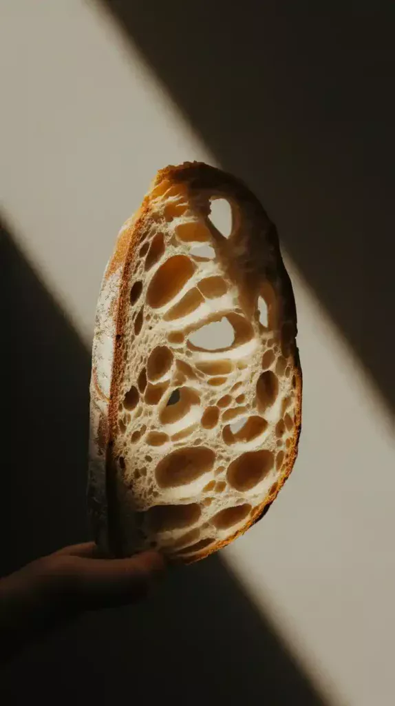 A close-up "crumb shot" of a slice of gluten-free sourdough bread, highlighting its airy and chewy internal texture.
