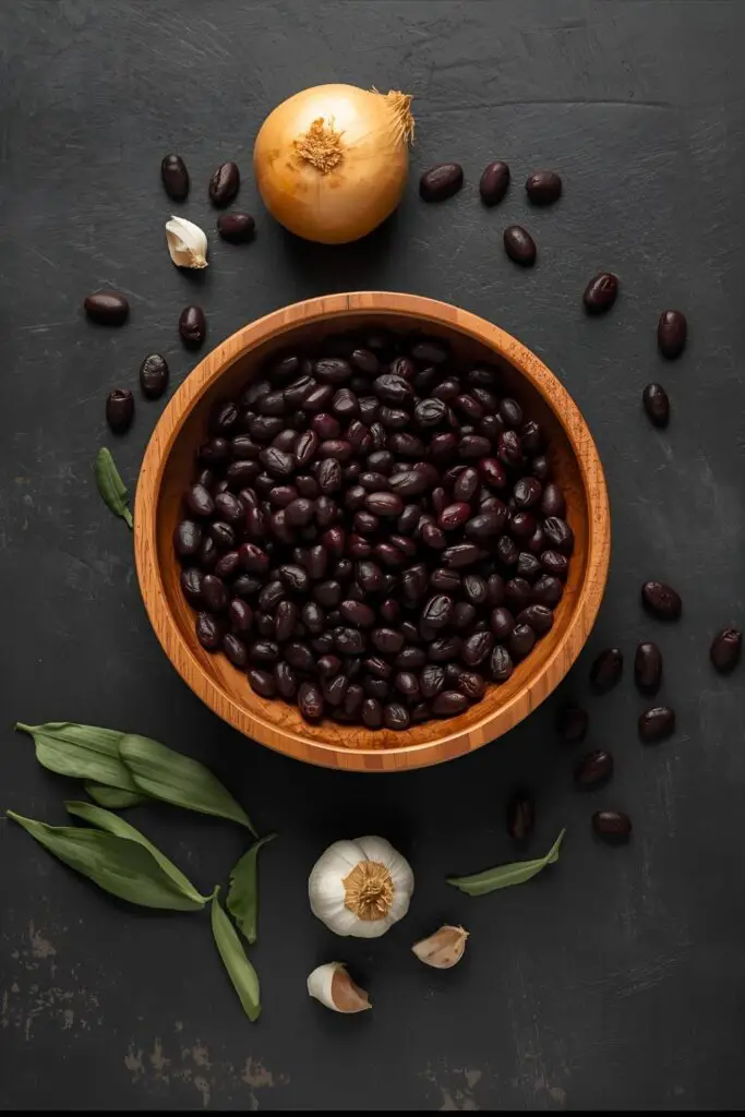 A flat lay of the simple ingredients for cooking dried black beans: beans, an onion, garlic, and a bay leaf.