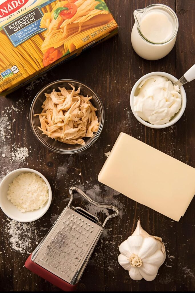 A flat lay of ingredients for chicken alfredo lasagna: noodles, chicken, cream, Parmesan, and ricotta.