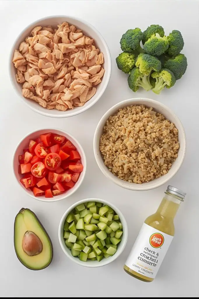 A flat lay of fresh and healthy ingredients for making chicken bowls: cooked chicken, quinoa, various chopped vegetables, and avocado.