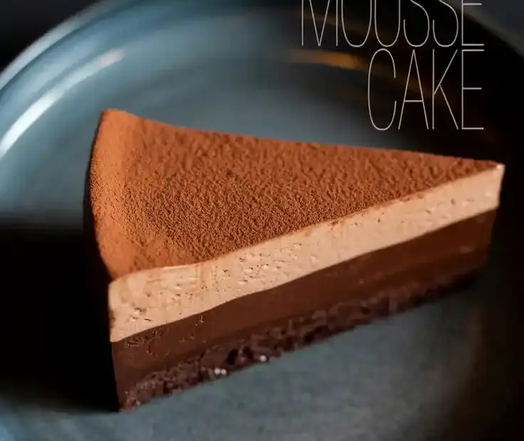 A slice of rich chocolate mousse cake on a dark plate, showing the flourless base and airy mousse layers.