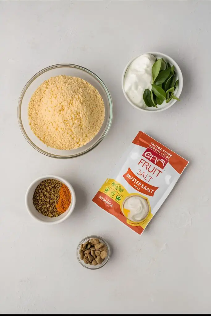 Flat lay of dhokla ingredients: gram flour, yogurt, spices, Eno, and tempering ingredients like mustard seeds and curry leaves.