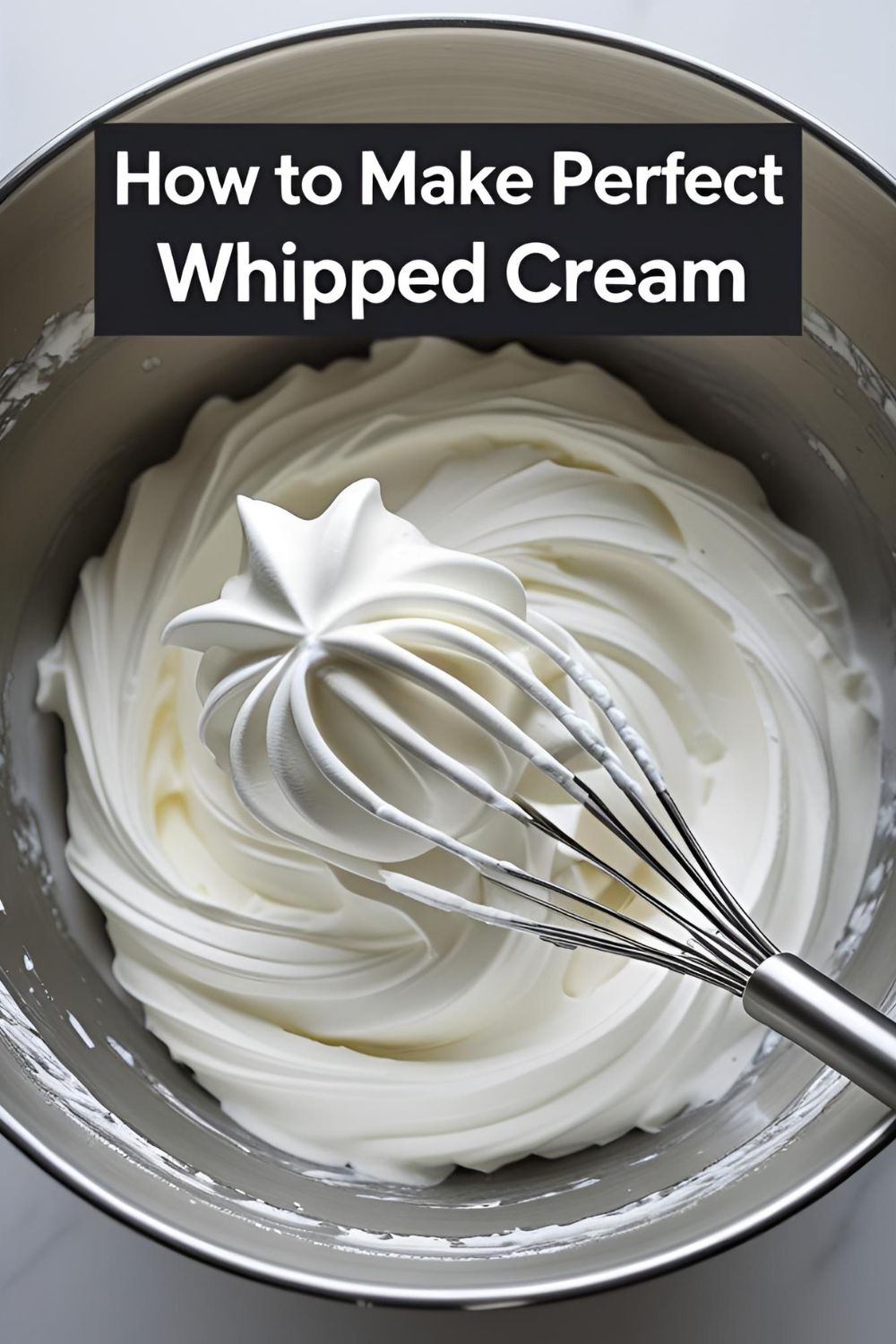 A metal bowl filled with thick, homemade whipped cream with stiff peaks, with a whisk resting inside.