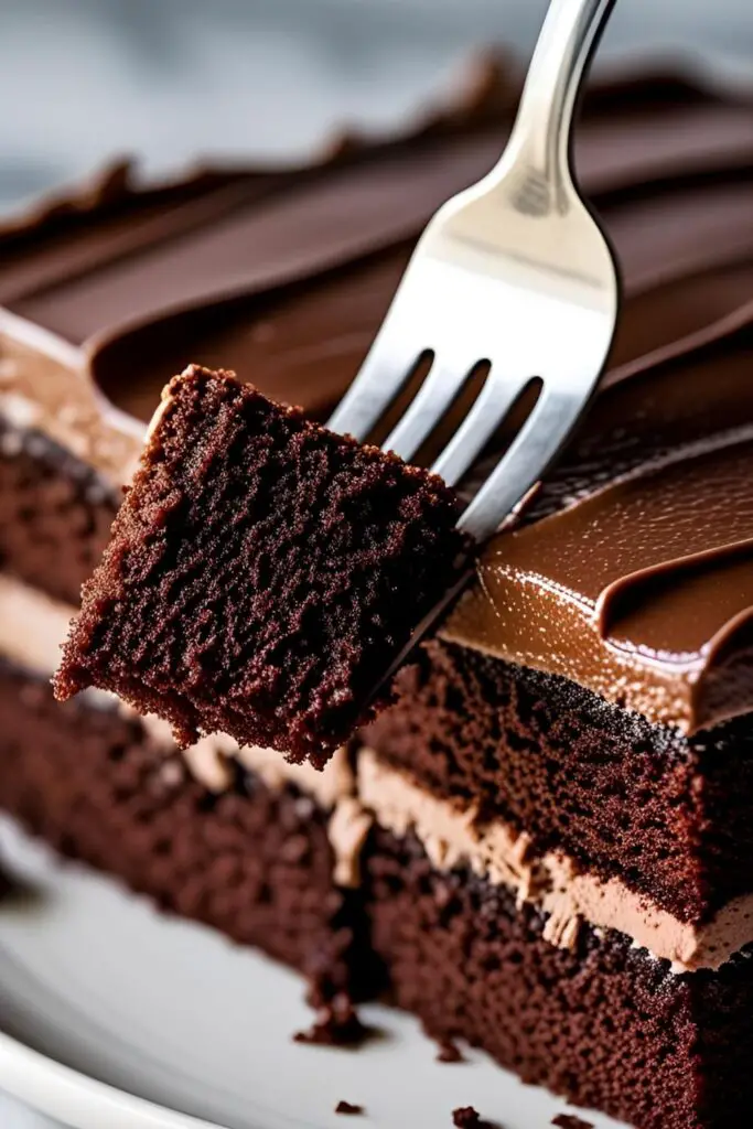 A close-up of a perfect slice of homemade moist chocolate layer cake, showing its tender crumb and fudgy frosting.