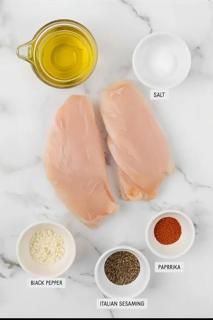 A flat lay of the simple ingredients for roasted chicken breast: chicken breasts, olive oil, and various dried spices.