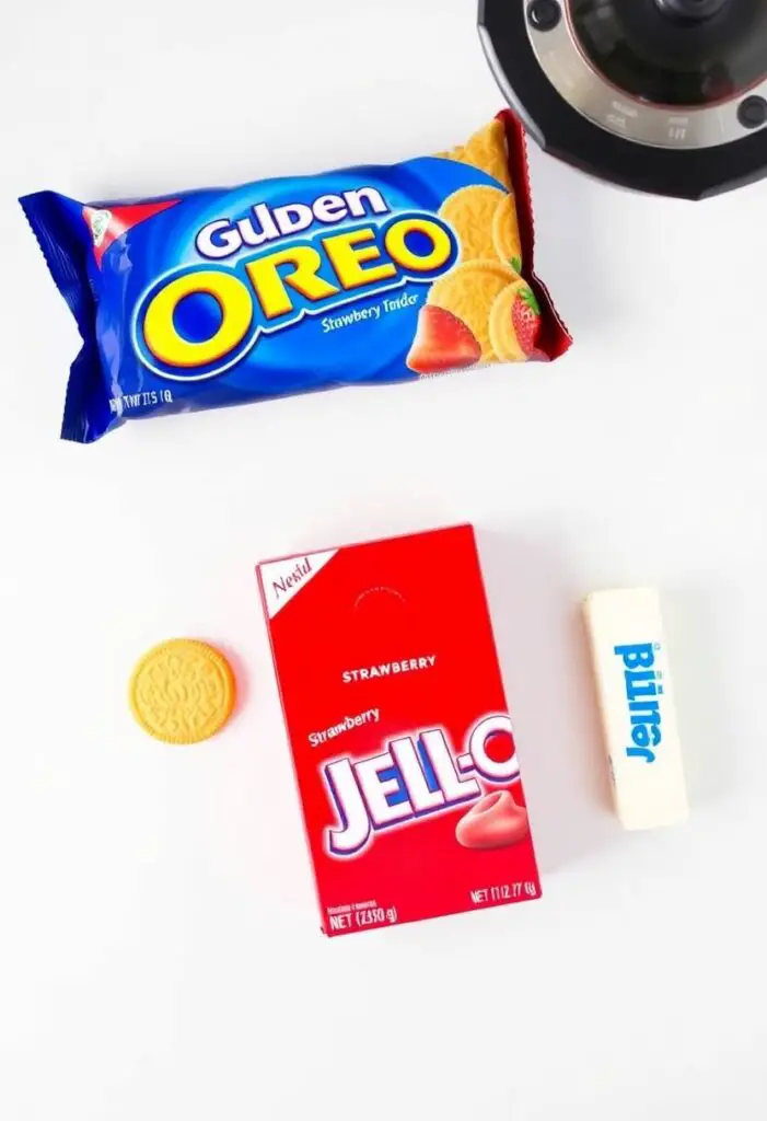 A flat lay of ingredients for strawberry shortcake crumble: Golden Oreos, a box of strawberry Jell-O, and a stick of butter.
