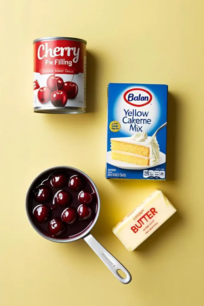 A flat lay of the three ingredients for a cherry dump cake: a can of cherry pie filling, a box of cake mix, and a stick of butter.