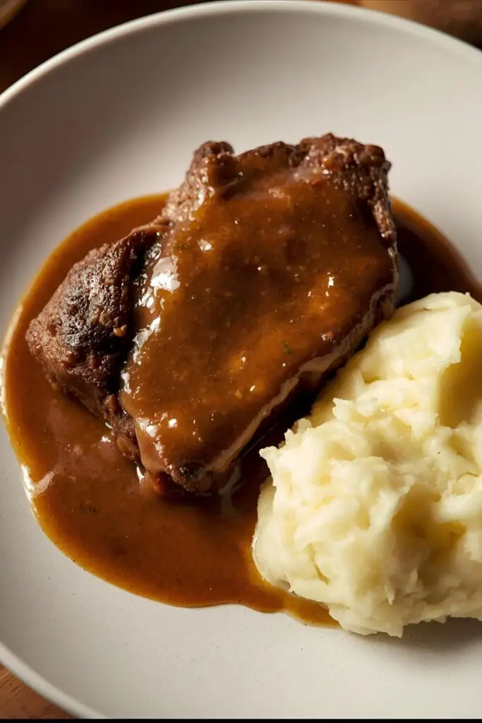 Text overlay "How to cook cube steak" on a background of a cooked cube steak with gravy